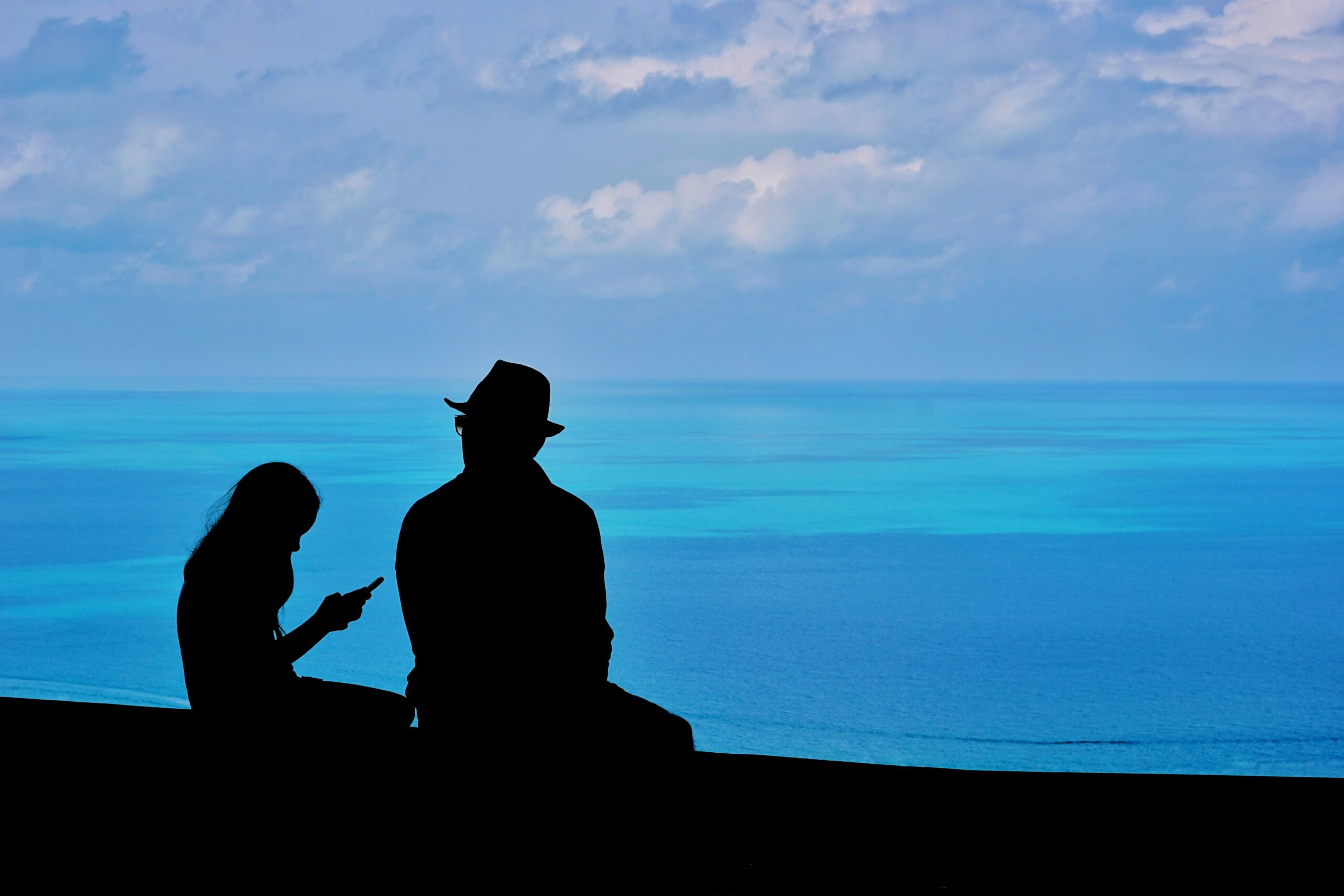 Photo of two people sitting by the ocean. One person is older and one is younger.